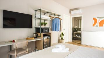 Habitación de hotel moderna con cama, escritorio con computadora, televisor, kitchenette y baño.