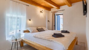 Ein Schlafzimmer mit einem hölzernen Bett, einem kleinen Tisch und einem Fenster mit transparenten Vorhängen.