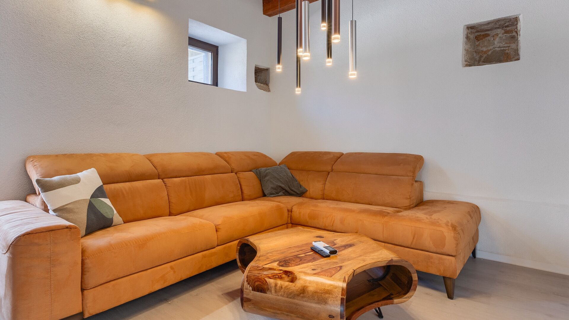 A modern living room with a leather sectional sofa, a wooden coffee table, and pendant lighting.