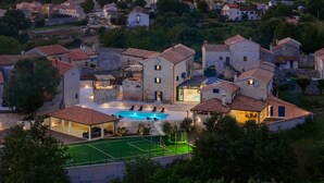 Eine Villa mit Swimmingpool, Tennisplatz und mehreren Gebäuden mit Steinmauern.