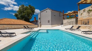 Ein Schwimmbecken mit Liegestühlen, ein Steinhaus und ein Ziegeldach.