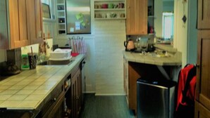 A compact kitchen with wooden cabinets, a stainless steel refrigerator, and a countertop with various kitchen items.
