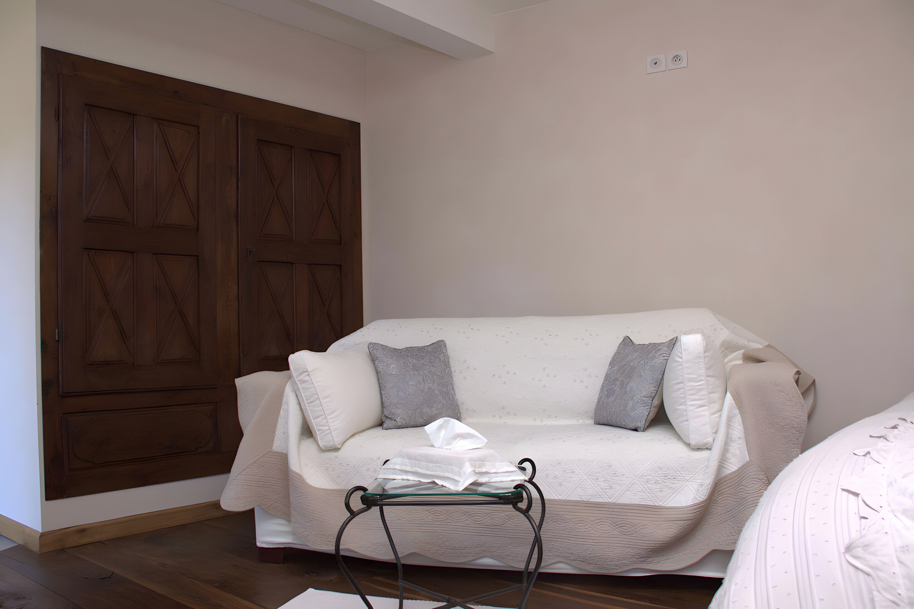 Ein Zimmer mit Holztür, einem weißen Sofa mit grauen Kissen und einem kleinen Tisch mit weißem Tuch.