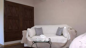 Ein Zimmer mit Holztür, einem weißen Sofa mit grauen Kissen und einem kleinen Tisch mit weißem Tuch.