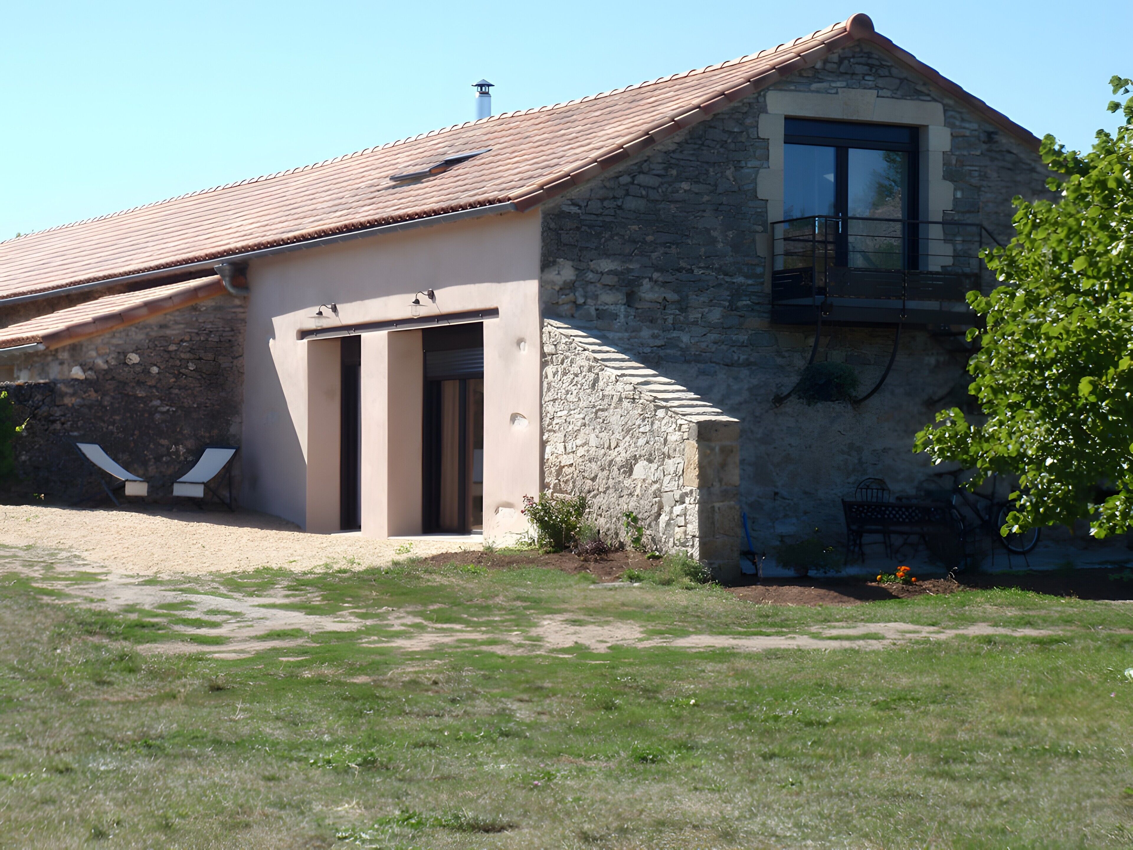 A stone building with a tiled roof, a balcony, and a door leading to a covered entrance.