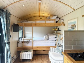 A bunk bed room with a loft bed, a small table, a chair, a sofa, a TV, and a painting on the wall. - Cosy luxury shepherd's hut, private garden, family & pet-friendly :) (Ditchingham)