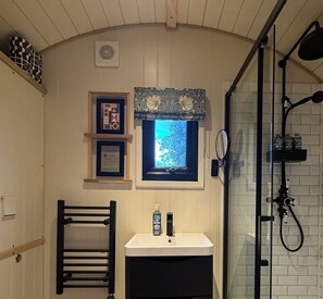 A bathroom with a shower, a small window, a sink, and a towel rack. - Cosy luxury shepherd's hut, private garden, family & pet-friendly :) (Ditchingham)