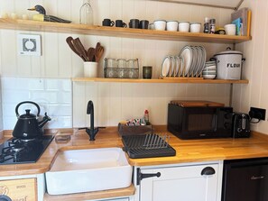 A kitchen with wooden shelves, a kettle, a toaster, and a microwave. - Cosy luxury shepherd's hut, private garden, family & pet-friendly :) (Ditchingham)