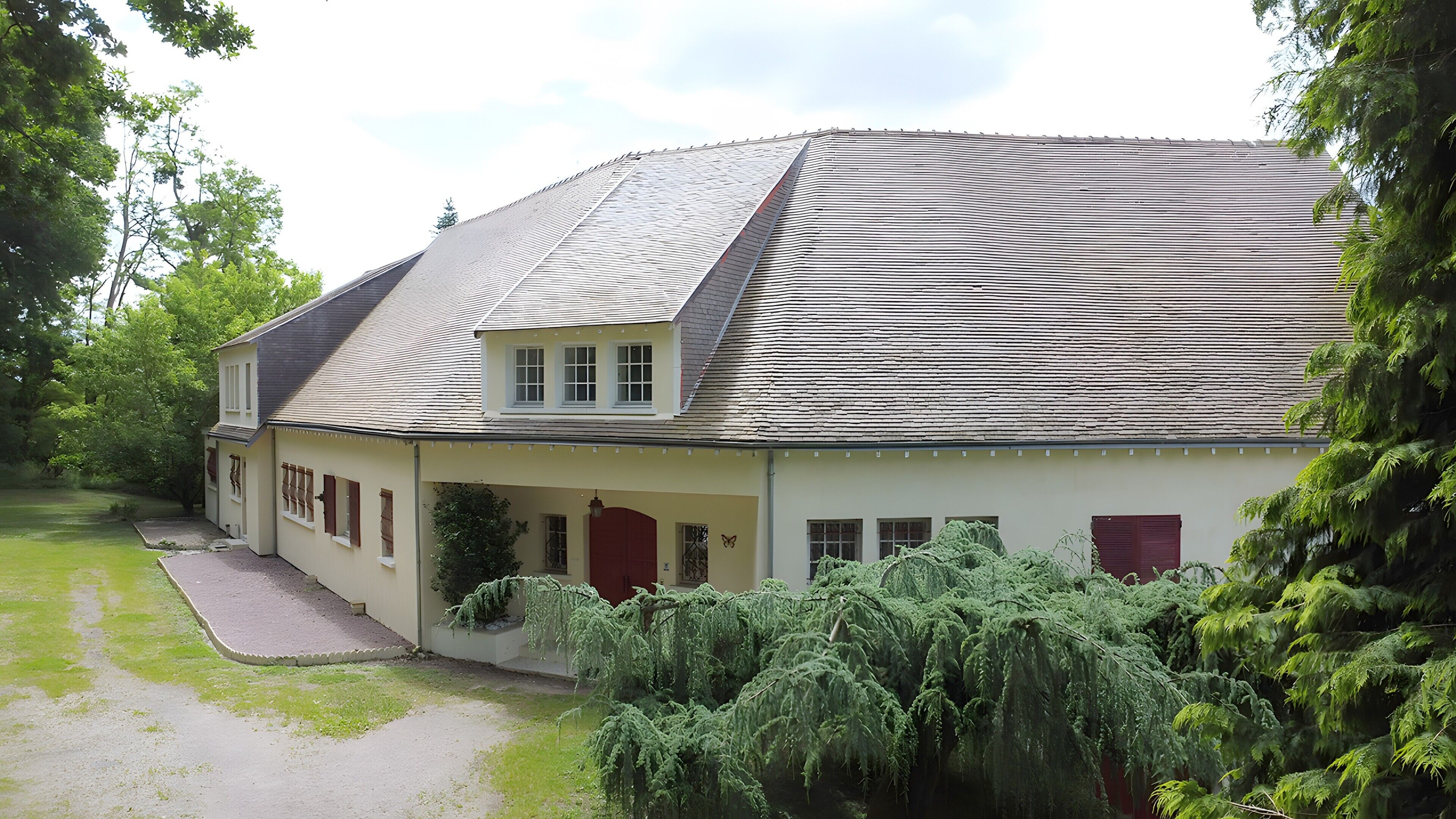 Een twee verdiepingen tellend huis met een schuin dak, een overdekte veranda en een verzorgd gazon.