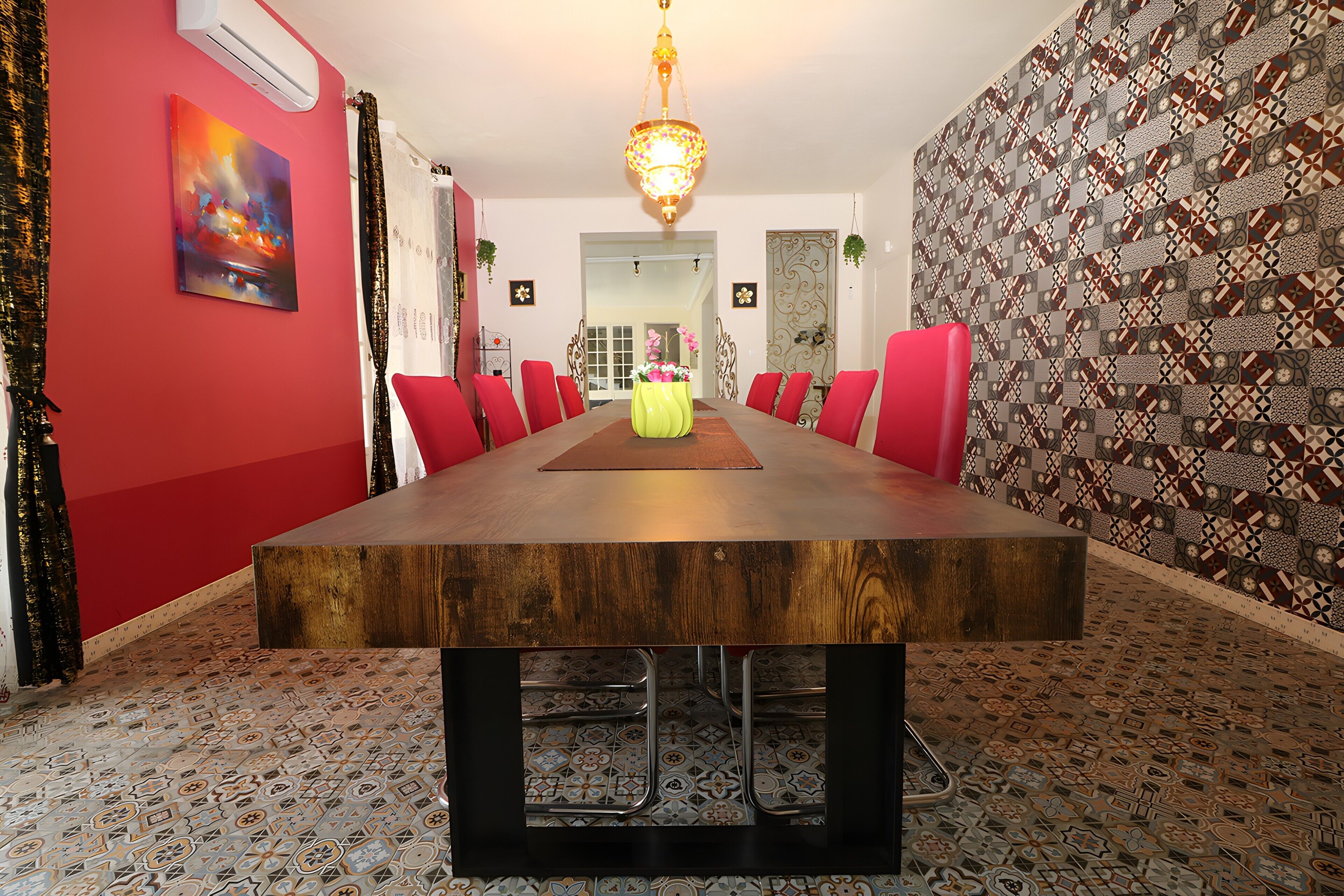 Un comedor con una larga mesa de madera, sillas rojas, una araña, papel tapiz estampado y una pared de acento roja.