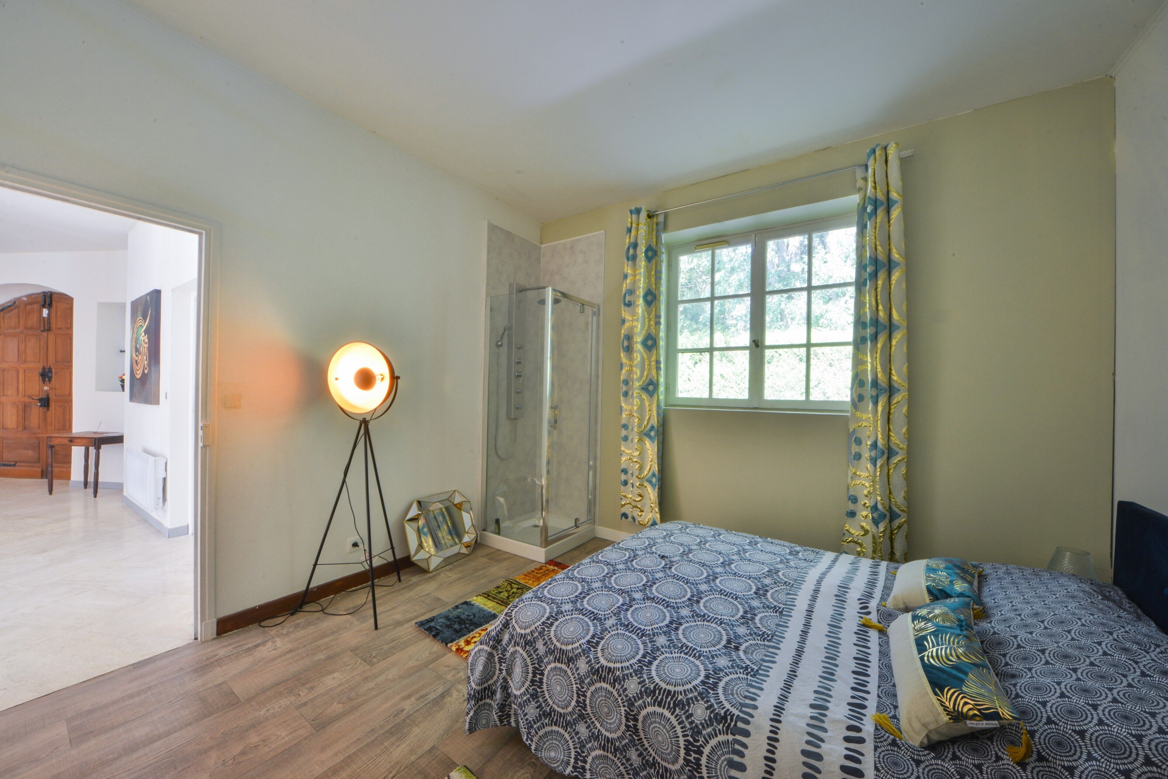 Une chambre à coucher avec un lit, une lampe sur pied, une douche et une fenêtre avec des rideaux.