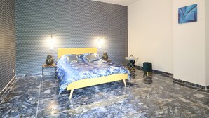 A bedroom with a patterned wall, a bed with a blue and white bedspread, two bedside lamps, and a modern light fixture. - Villa 'Alhambra' with Private Terrace, Wi-Fi and Air Conditioning (Vierzon)