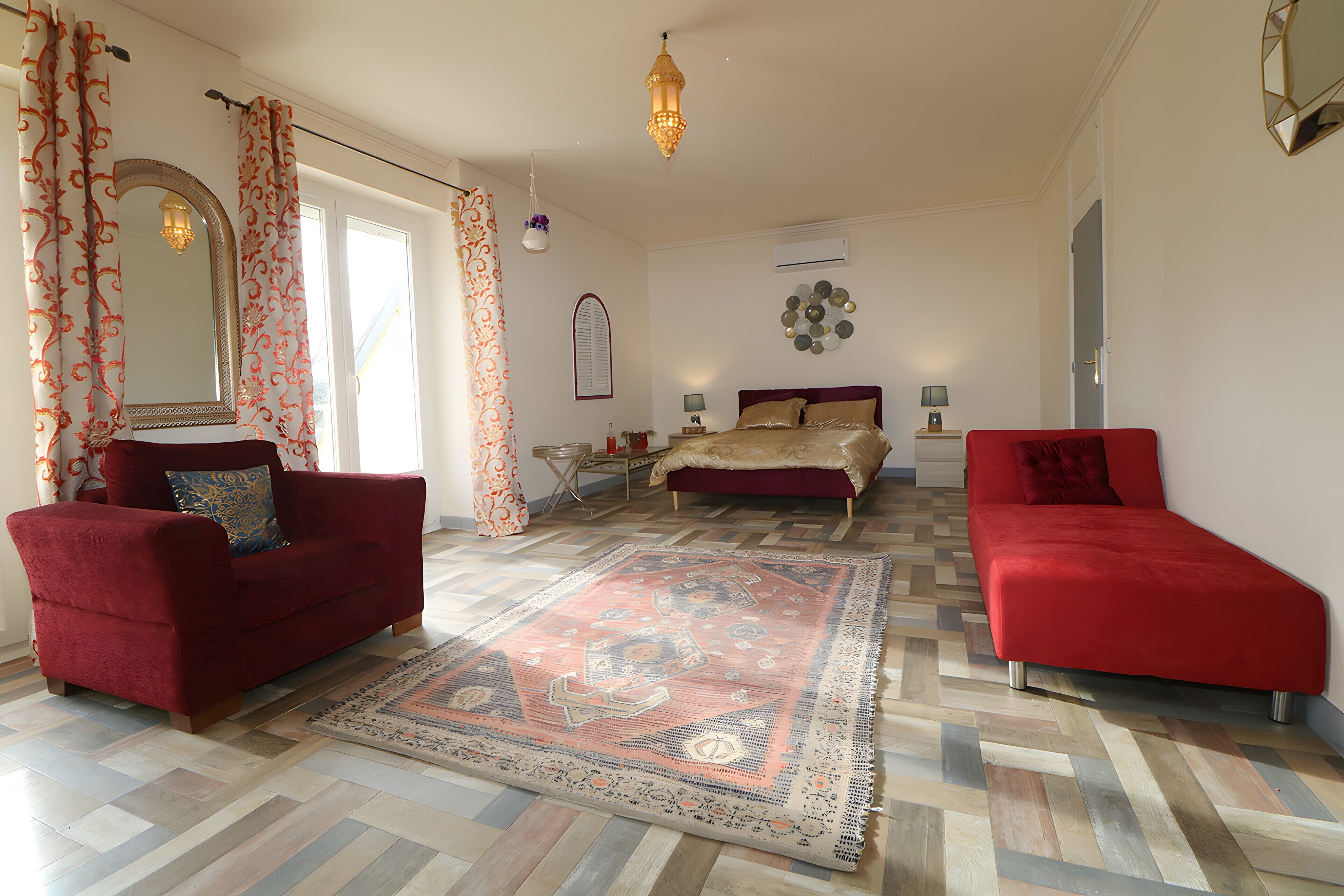 A spacious room with a large bed, two red sofas, a patterned rug, and a chandelier.