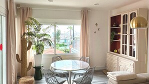 En moderne stue med et rundt spisebord, en sofa, et skab og et stort vindue med gardiner.