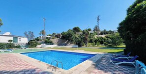 Ein Swimmingpool mit klarem, blauem Wasser, umgeben von einem Schachbrettmuster aus Fliesen und einer Rasenfläche mit Liegestühlen.