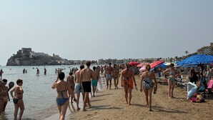 En strand med folk, parasoller og en borglignende bygning i baggrunden.