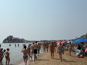 Ein Strand mit Menschen, Sonnenschirmen und einer baukastelnähnlichen Struktur im Hintergrund.