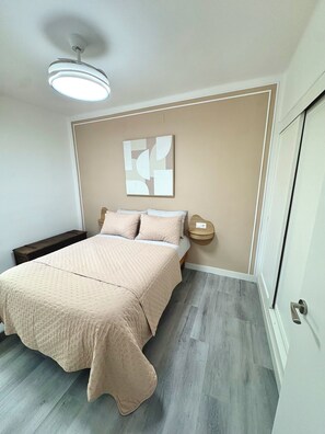 Ein Schlafzimmer mit einem Bett, Nachttischen, einer Deckenleuchte und einem an der Wand befestigten, abstrakten Kunstwerk.