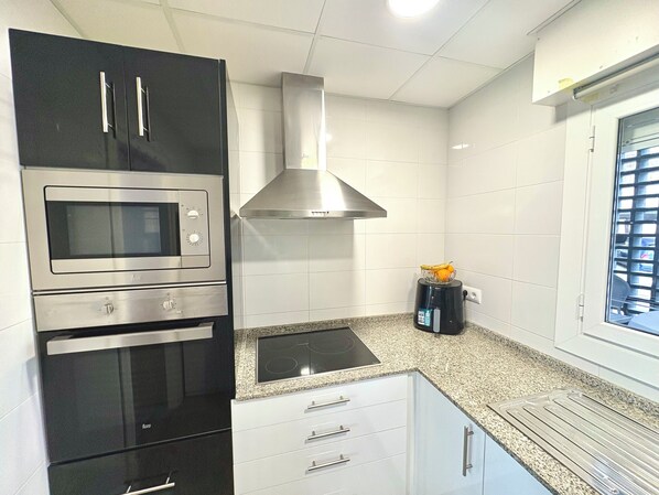 A kitchen with a built-in oven, microwave, and stove, a stainless steel range hood, and a window with blinds. - Oasis with panoramic views of the Mediterranean, a pool, and private parking (Peñiscola)
