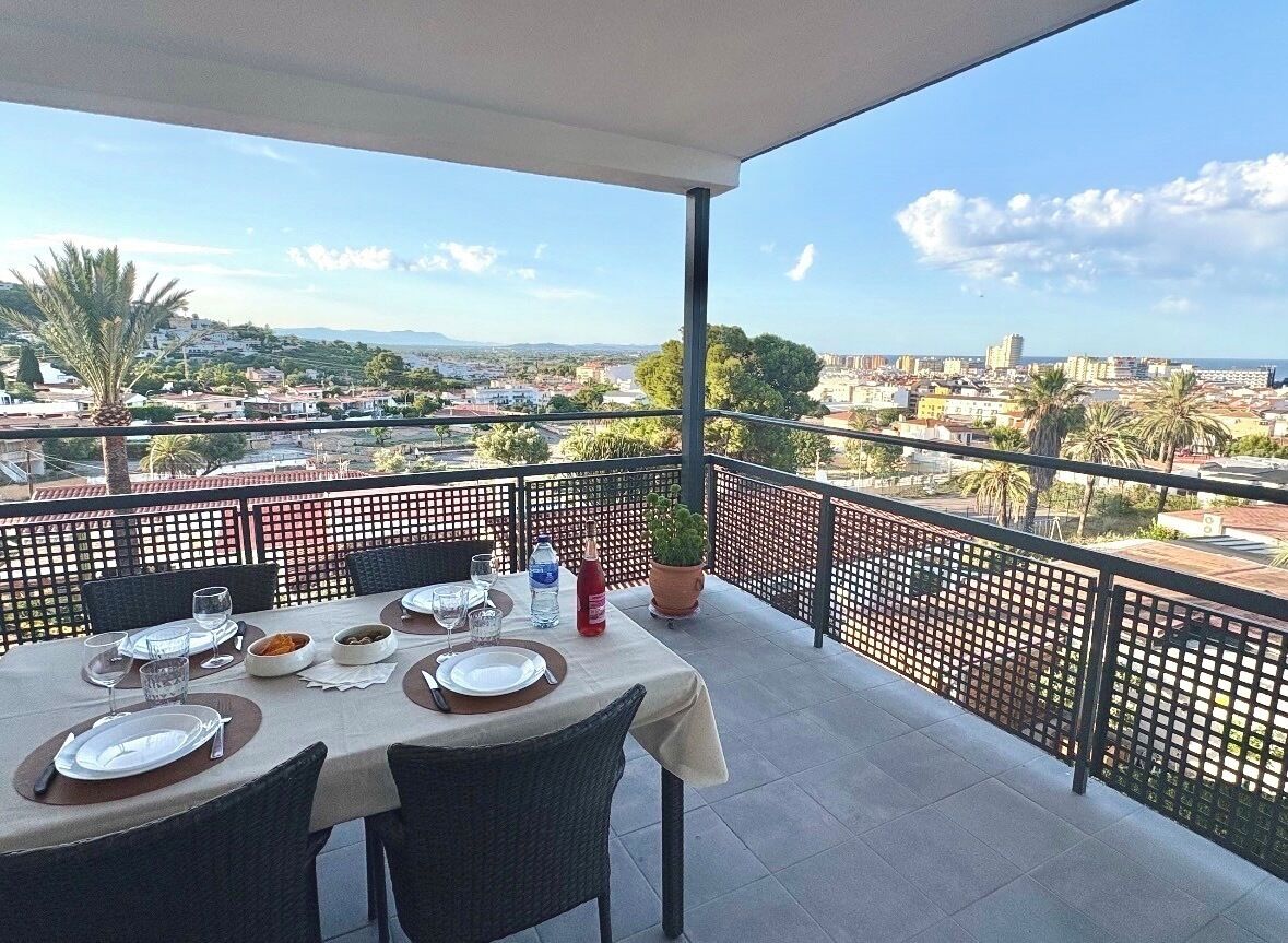 A balcony with a table set for dining, overlooking a cityscape with buildings and palm trees.