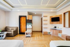 Habitació d'hotel moderna amb un sòl de fusta en disseny de guillots, un sofà de pell, un llit, una taula petita, un televisor fixat a la paret i armaris de fusta integrats.