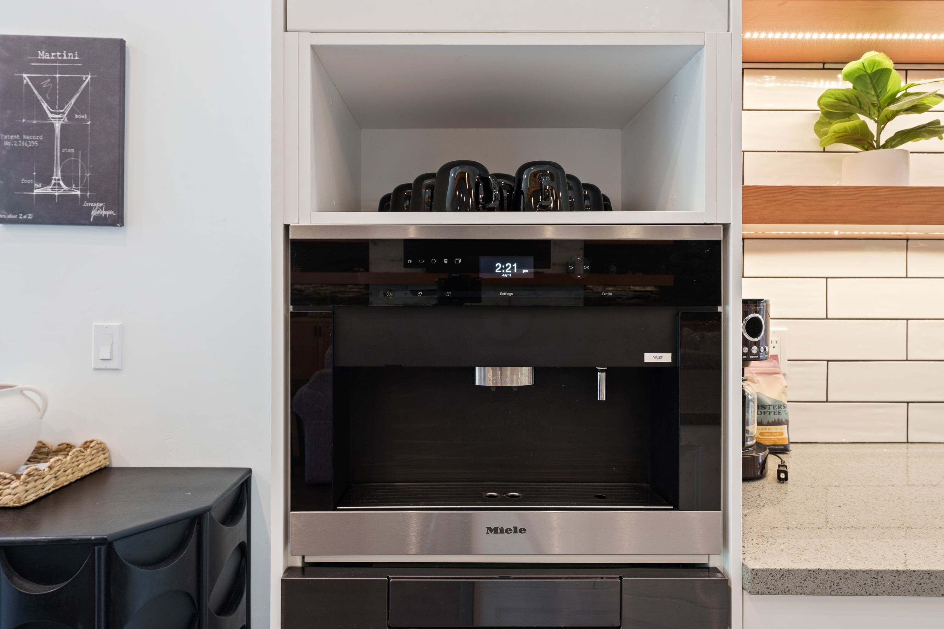 A modern kitchen with a coffee machine, a clock displaying 2:21, and a plant on the counter.