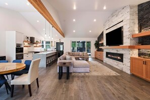 A modern kitchen with a central island, a dining area with a round table and chairs, a living room with a sectional sofa, and a fireplace. - 9 Lassen - Modern , Hot Tub, Luxury, 12 SHARC Passes (Sunriver)