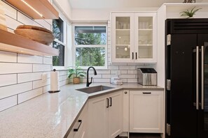 Eine Küche mit weißen Schränken, einem schwarzen Kühlschrank, einem Fenster und einer Arbeitsplatte mit Spüle.