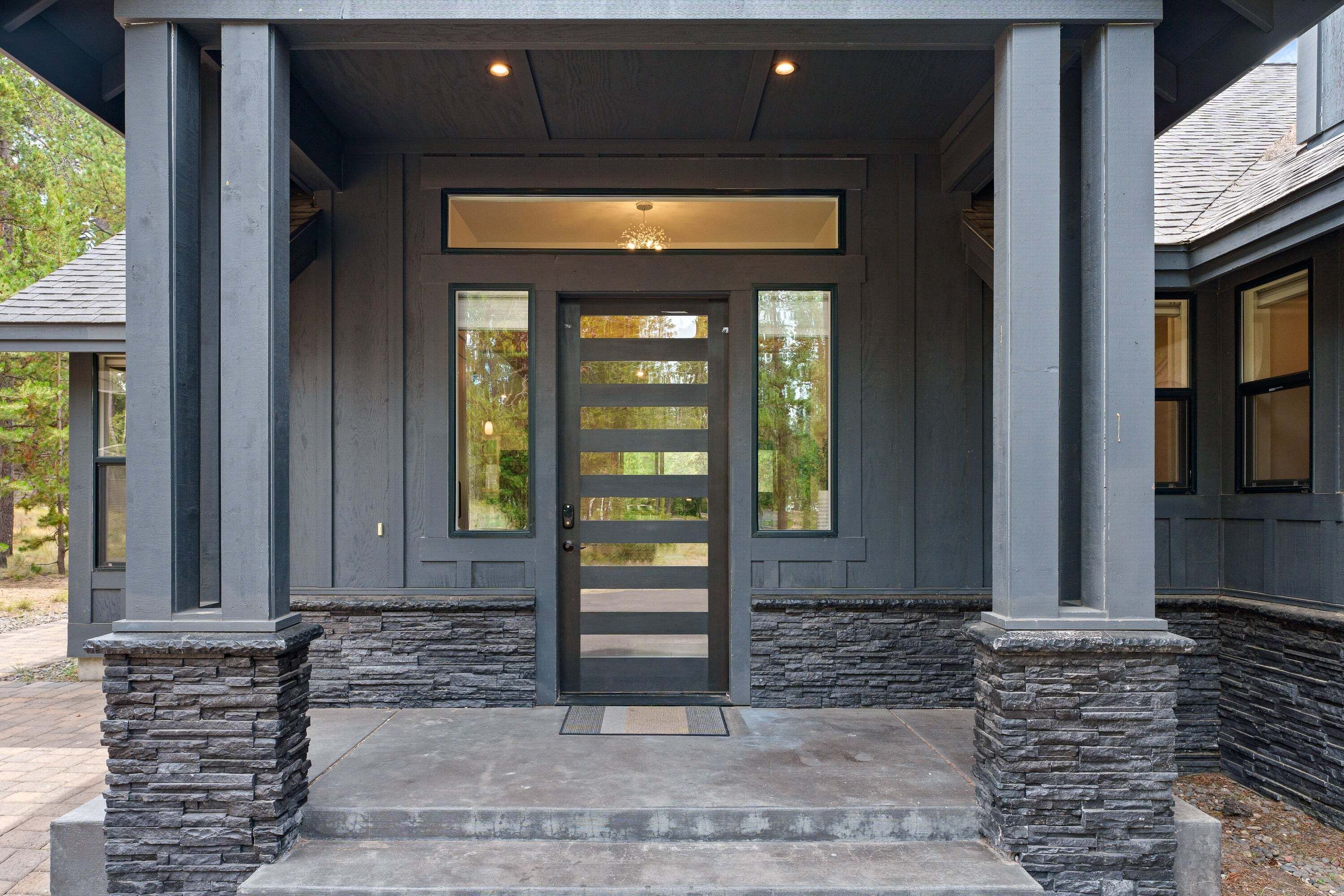 A modern house entrance with a dark facade, stone accents, and a glass door with a horizontal stripe pattern.