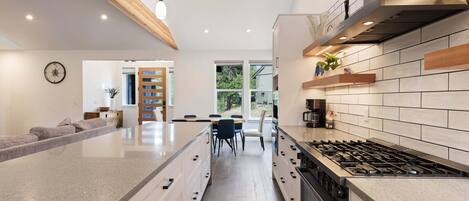 A modern kitchen with a central island, a dining area, and a view of the outdoors.