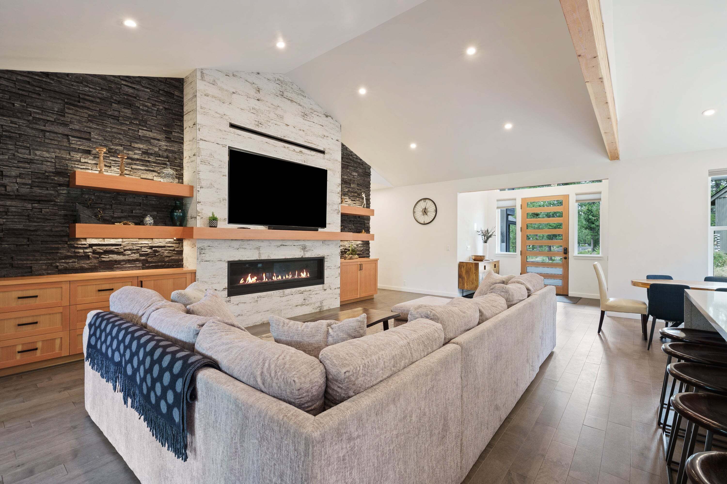 A modern living room with a stone fireplace, a flat-screen TV, and a large L-shaped sectional sofa.