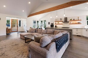 A spacious living area with a large sectional sofa, a dining table, and a kitchen with white subway tiles and wooden accents. - 9 Lassen - Modern , Hot Tub, Luxury, 12 SHARC Passes (Sunriver)