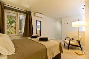 Ein Hotelzimmer mit einem Bett, einem Sessel, einer Lampe, einer Klimaanlage und einem Vorhangfenster.
