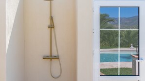 A showerhead mounted on a wall with a window view of a pool and palm trees. - Guesthouse 'Casita Chupito' with Mountain Views, Wi-Fi and Air Conditioning (Alozaina)