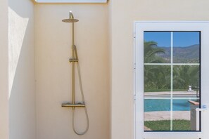 Eine Duschbrause an der Wand, mit Blick aus dem Fenster auf einen Pool und Palmen.