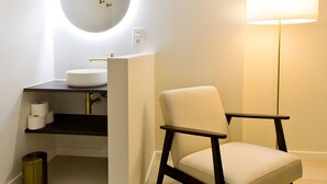 A modern bathroom with a round mirror, a sink, a chair, and a floor lamp. - Guesthouse 'Casita Chupito' with Mountain Views, Wi-Fi and Air Conditioning (Alozaina)