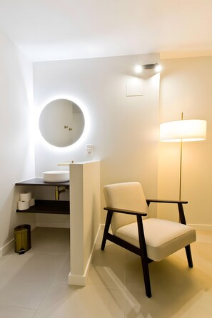 A modern bathroom with a round mirror, a sink, a chair, and a floor lamp.