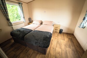 Ein Schlafzimmer mit einem Doppelbett, einem Nachttisch mit Lampe, einer Heizung und einem Fenster mit Vorhängen.