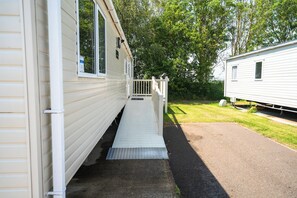 A mobile home with a ramp leading to a porch, surrounded by trees. - Cosy Modern 2-Bed Caravan Near Skegness Beach (Skegness)