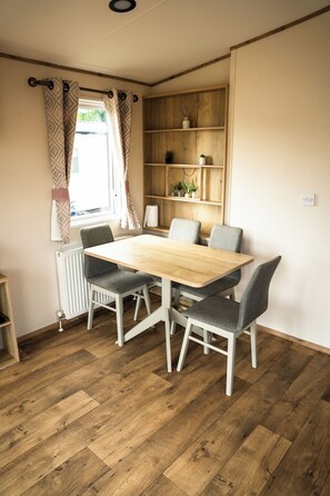 Ein Essbereich mit Holztisch und grau gepolsterten Stühlen, einem Heizkörper und einem Holzregal mit Pflanzen.