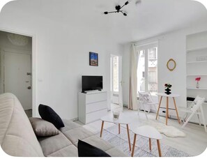Ein modernes Wohnzimmer mit einer Couch, einem Fernseher, einem kleinen Tisch und einem Sessel.