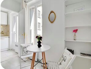 Ein heller Raum mit einem runden Tisch, einem Stuhl, einem Heizkörper, einem Spiegel und einem Regal mit einer Vase.