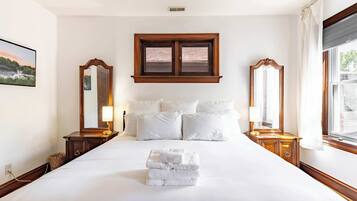 A hotel room with a large bed, two nightstands, a mirror, a window with curtains, and a picture on the wall.
