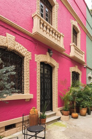 A building with a pink facade, a black door, and a small balcony. - Chic 3-bedroom townhouse in heart of Roma Norte (Ciudad de México)