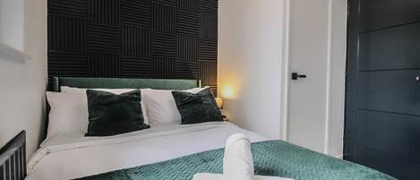 Quarto de hotel com cama, almofadas, um edredom verde e uma toalha enrolada.