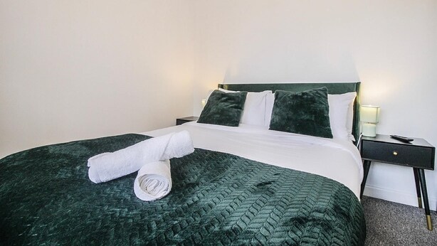 A neatly made bed with a green quilt, white linens, and a rolled white towel. - Hockley 4-bed, Sleeps 13 w/ Garden & Free Parking (Birmingham)