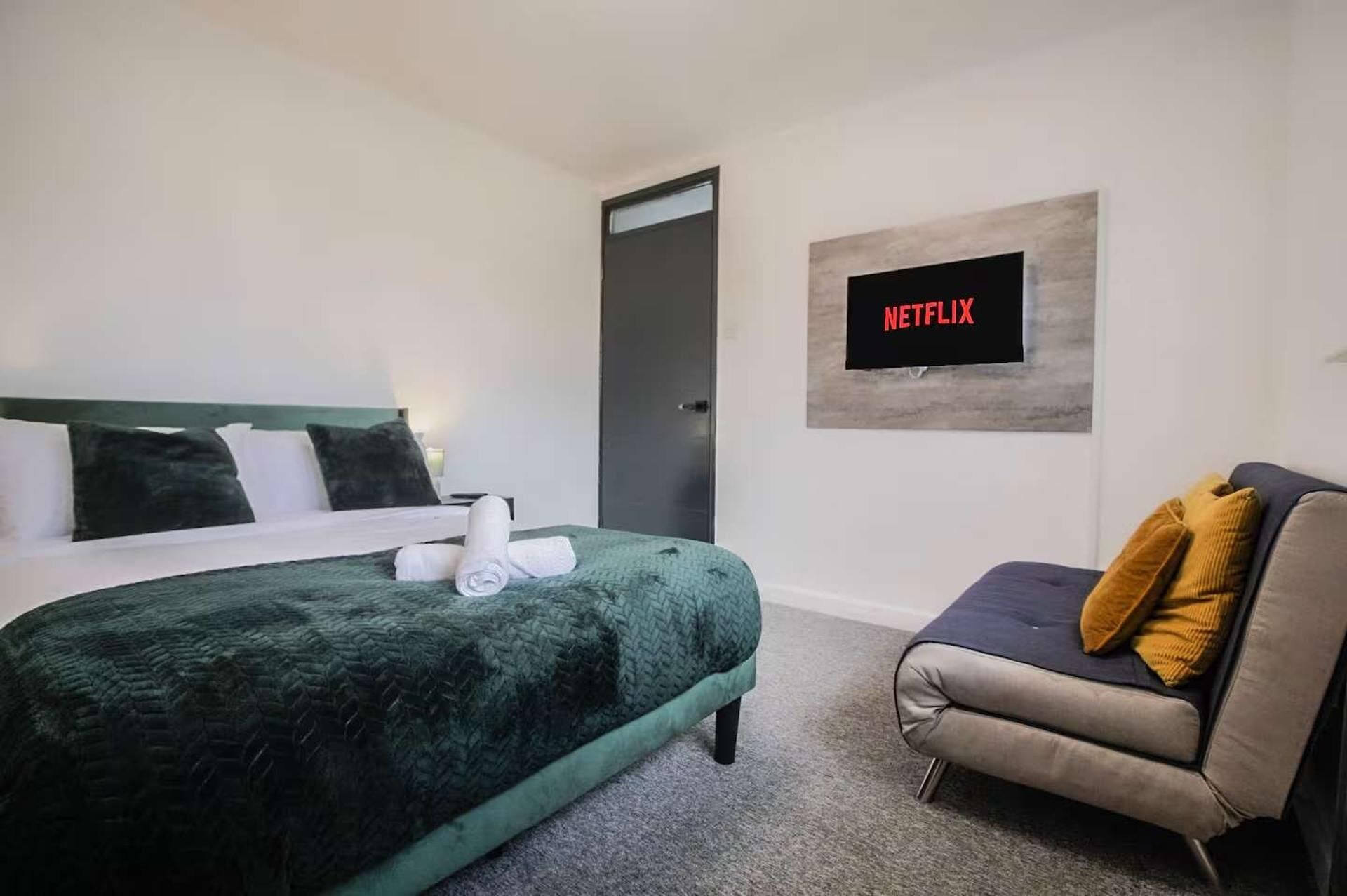 A hotel room with a bed, a sofa, a television mounted on the wall, and a door.