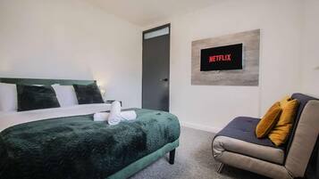 A hotel room with a bed, a sofa, a television mounted on the wall, and a door.