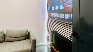 A living room with a grey sofa, a flat-screen TV mounted on a wall with a striped pattern, and a fireplace with a decorative item. - Hockley 4-bed, Sleeps 13 w/ Garden & Free Parking (Birmingham)