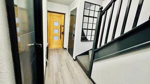 A hallway with a wooden door, a window with a grid pattern, and a staircase with black railings. - Hockley 4-bed, Sleeps 13 w/ Garden & Free Parking (Birmingham)